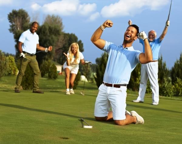 Happy golfer kneeling at hole with raised fists after putting in